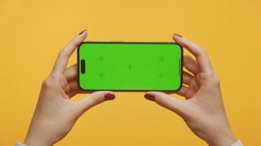 Sarı arkaplanda yeşil ekranlı akıllı telefonu tutarak yakınlaştır