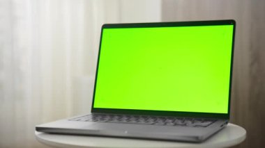 Dolly zoom tarafında yeşil ekranlı bir dizüstü bilgisayar yumuşak ışıklandırılmış bir iç mekan ortamında, arka planda sadece perdeler olan yuvarlak beyaz bir masa üzerine yerleştirilmiş.