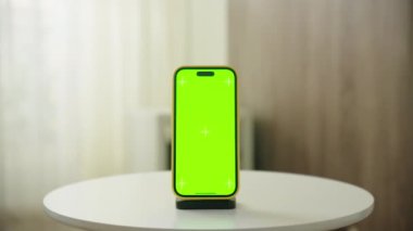 Akıllı bir telefondan, yeşil bir ekranla, yuvarlak beyaz bir masanın üzerine, arka planda perdelerle birlikte, yumuşak bir şekilde aydınlatılmış bir iç mekan ortamında uç.
