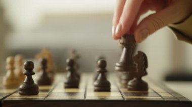 Bir el yakın plan satranç tahtasında tahta bir taşı hareket ettiriyor, stratejik oyun üzerine odaklanıyor.