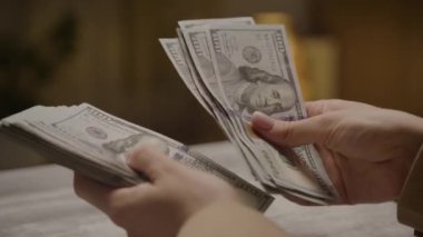 Yakın plan çekimleri, arka planı bulanık yüz dolarlık banknotları sayıyor.