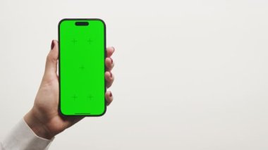 Sade beyaz bir arkaplana karşı yeşil ekranlı akıllı telefonu tutan bir elin yakın çekimi