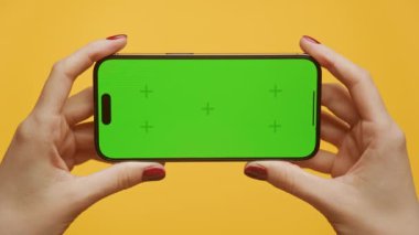 Eller, yeşil ekranlı akıllı telefonu canlı sarı bir arka plana yatay olarak tutuyor.