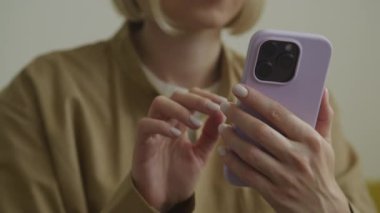 Mor çantalı akıllı telefon kullanan bir kadının yakın çekimi. Ellerine ve cihaza odaklanmış.