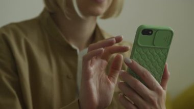 Yeşil çantalı akıllı telefon kullanan bir kadın, ellerine ve cihazına odaklanıyor.