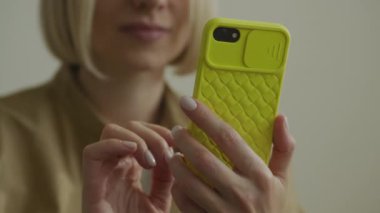 Parlak sarı çantalı akıllı telefon kullanan bir kadının yakın plan fotoğrafı. Ellerine ve telefonuna odaklanmış.