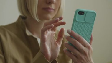 Açık mavi çantalı akıllı telefon kullanan bir kadının yakın plan fotoğrafı. Ellerine ve telefonuna odaklanmış.