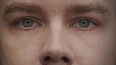 Mavi gözlerin açılıp kameraya baktığı, detaylı yüz hatları ve ifadelerini gösteren bir kişinin yakın plan fotoğrafı.