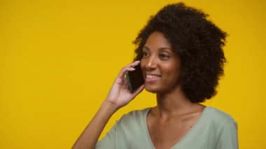 Kıvırcık saçlı bir kadın telefonda konuşurken gülümsüyor.