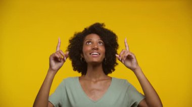 Heyecanlı bir kadın iki eliyle yukarı bakıyor, sarı bir arka plana gülümsüyor.