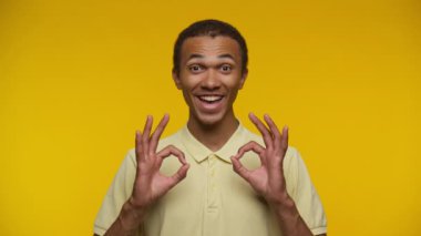 Sarı tişörtlü mutlu adam sarı arka planda iki eliyle işaret veriyor.