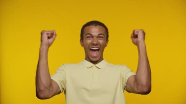 Sarı tişörtlü mest olmuş bir adam sarı arka planda iki eli havada tezahürat yapıyor.