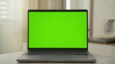 Yeşil ekranlı dizüstü bilgisayar ve yumuşak ışıklandırılmış bir odadaki masanın üzerindeki boşluğu kopyala
