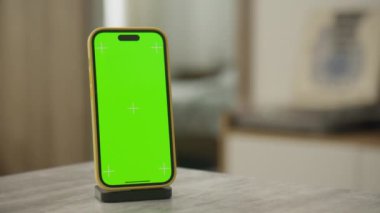 Smartphone 'un etrafında dönen yeşil ekran yumuşak ışıklı bir odada duruyor.