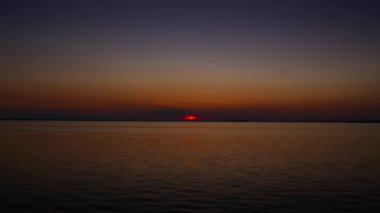 Sakin suyun üzerinde canlı renklerle sakin bir günbatımı, sakin ve huzurlu bir manzara yaratır.