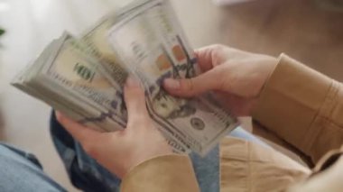 Arkaplanı bulanık olan 100 dolarlık banknotları sayan eller.