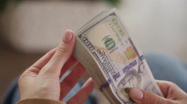 Yakın plan çekimleri, arka planı bulanık yüz dolarlık banknotları tutuyor.