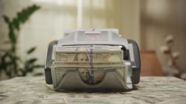 Para sayma makinesi ön planda dağınık banknotlarla Amerikan doları banknotlarını işliyor.