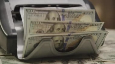 100 dolarlık banknotları sayan para sayma makinesinin yakın plan çekimi.
