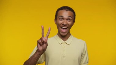 Neşeli adam elini sarı bir arka plana koyup barış işareti yapıyor.