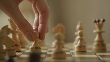 Satranç tahtasında satranç piyonunu hareket ettiren bir elin yakın çekimi stratejiyi ve oyunun odak noktasını vurgular.