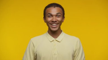 Neşeli bir ifadeyle başarıyı kutlayan genç adam, sarı bir arka plana karşı heyecanla yumruğunu sıkıyor.