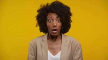 Şaşırmış bir kadın, geniş gözlü ve ağzı açık, şok ya da şaşkınlık ifade eden, canlı sarı bir arka planda