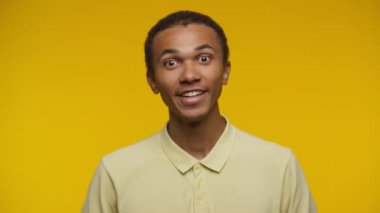 Sarı polo tişört giyen neşeli bir gencin portresi. Güvenle başını sallıyor. Açık sarı bir arka plana doğru.