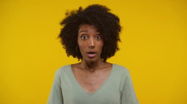 Doğal kıvırcık saçlı genç bir kadının portresi, ağzı hafifçe açık, canlı sarı bir arka planda duran, şaşırmış görünüyordu.