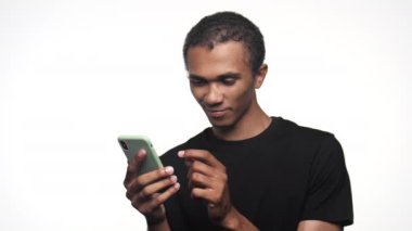 Siyah tişörtlü genç bir adam elinde akıllı bir telefon, derin düşüncelere dalmış, beyaz bir arka planda izole edilmiş.