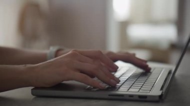 Dizüstü bilgisayarda yazı yazan ellerin yan görünüşü, loş bir odada odak ve verimliliği vurguluyor.