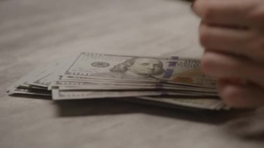 Masadaki Amerikan doları banknotlarını sayarak, mali işlemleri, tasarrufları ve nakit akışını temsil eden bir elin yakın çekimi
