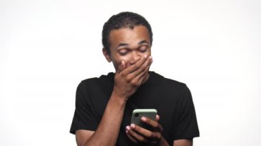 Mutlu bir genç adam, akıllı telefonuna bakıp heyecanını dile getirirken elini kaldırarak kutluyor.