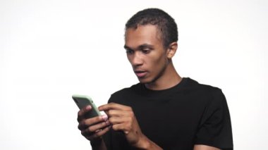 Genç bir adam akıllı telefonuna bakarken, beklenmedik haberlere tepki göstererek ağzını şoka sokuyor.
