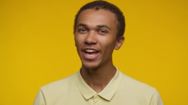 Genç bir adam parmağını dudaklarına dayayıp sarı bir arka plana karşı sessizlik işareti veriyor..