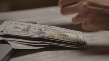 Zenginliği ve finansmanı temsil eden 100 dolarlık banknotları sayan bir elin yakın çekimi..