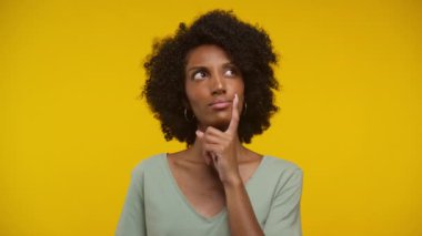Kıvırcık saçlı kadın, derin düşüncelere dalmış, parmakları çenesinde, canlı sarı bir arka planda