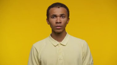 Sarı gömlekli genç bir adam, sarı arka planda, şaşırmış bir ifade sergiliyor..