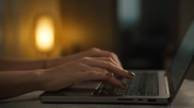 Yumuşak, sıcak ışıklandırmayla aydınlatılmış rahat bir çalışma alanında dizüstü bilgisayarda yazı yazan eller..