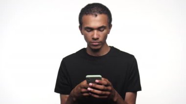 Akıllı telefon tutan genç bir adam ve omuz silkerek sırıtıyor, beyaz bir arka planda izole edilmiş..