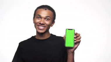 Mutlu adam yeşil ekranlı akıllı telefonu gösteriyor ve beyaz arka planda izole edilmiş bir şekilde baş parmağını kaldırıyor..