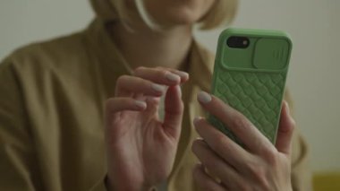Yeşil desenli bir çantayla akıllı telefonu tutan bir kadının elleri ekranı tıkırdatıyor.