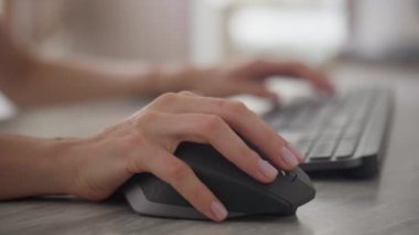 Ofis işlerini ve teknoloji kullanımını temsil eden, arka planda klavyesi olan kablosuz bir fare kullanan bir elin yakın çekimi