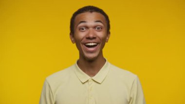 Heyecanlı ve şaşırmış bir ifadeyle genç bir adam, sarı bir gömlek giyiyor, parlak sarı bir arka planı var.