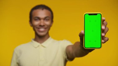 Genç adam elinde yeşil ekranlı bir akıllı telefon tutarken gülümsüyor. Krom anahtar için uygun, sarı arka plan.
