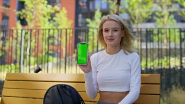 Gülümseyen ve elinde yeşil ekranlı bir akıllı telefon tutan genç bir kadın.