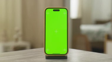 Krom anahtar kullanımı için kenetlenme standında duran yeşil ekranlı akıllı telefon, rahat bir ev ortamında