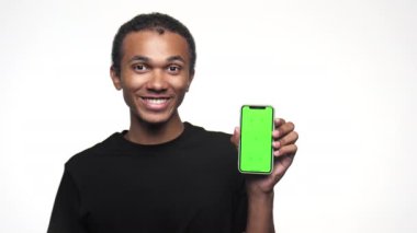 Siyah tişörtlü genç bir adam gülümsüyor, elinde yeşil ekranlı bir akıllı telefon var ve başparmağını kaldırıyor.