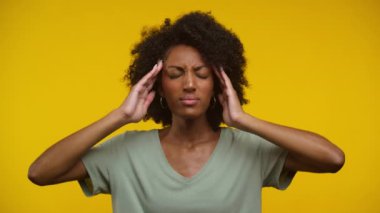 Kıvırcık saçlı, gözleri kapalı, parlak sarı bir arka plana karşı duran, hayal kırıklığı içinde başını tutan genç bir kadın.