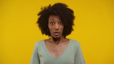 Sarı arka planda duran kıvırcık saçlı ve şok olmuş bir genç kadın.